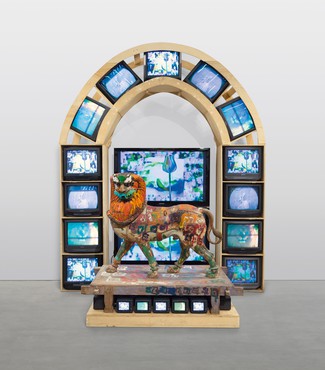彩绘的木狮子雕塑站在木底座上，电视显示器显示下面和后面的彩色视频