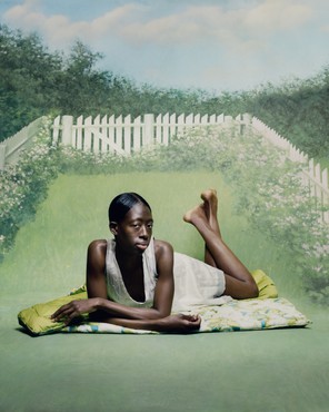 一个黑人妇女趴在草地上的毯子上，周围是白色的尖桩篱笆